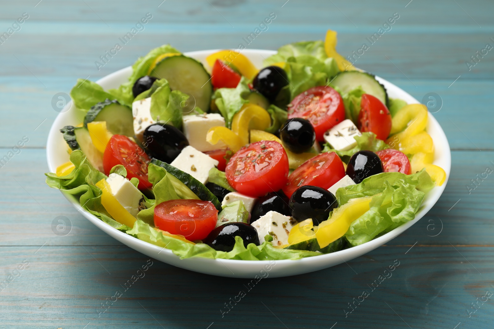 Photo of Delicious fresh Greek salad on light blue wooden table, closeup