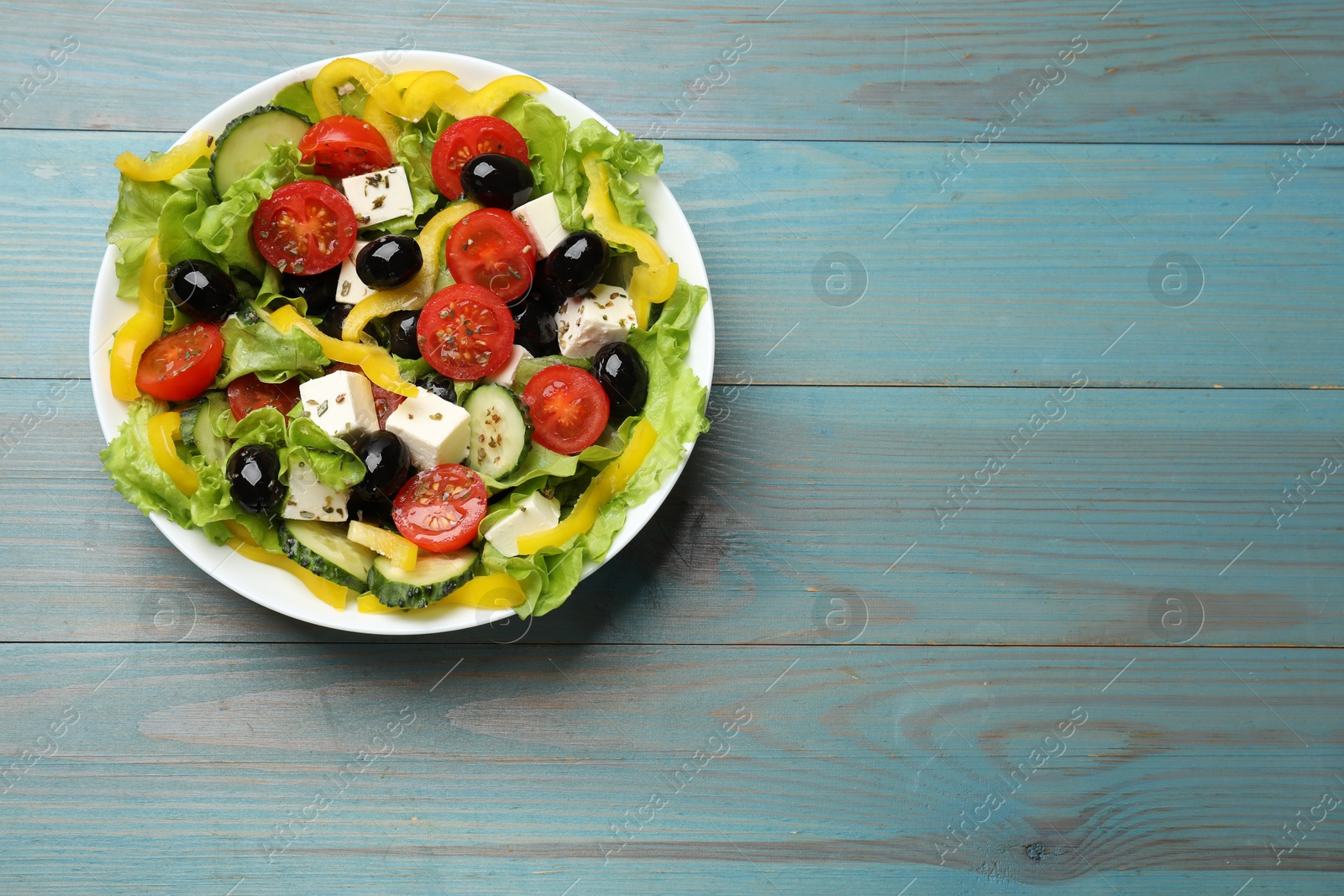 Photo of Delicious fresh Greek salad on light blue wooden table, top view. Space for text