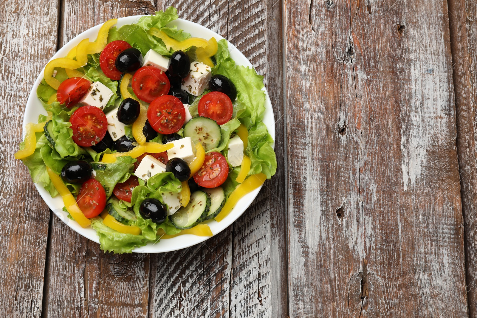 Photo of Delicious fresh Greek salad on wooden table, top view. Space for text