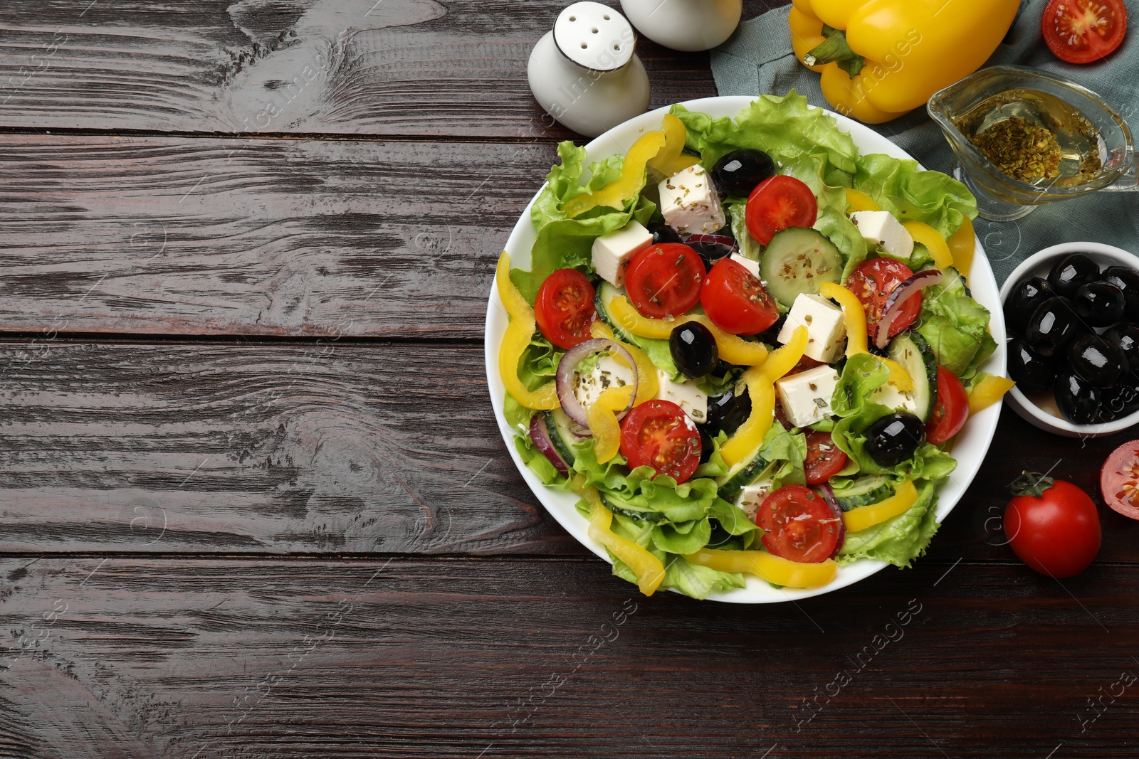 Photo of Delicious fresh Greek salad and ingredients on wooden table, flat lay. Space for text