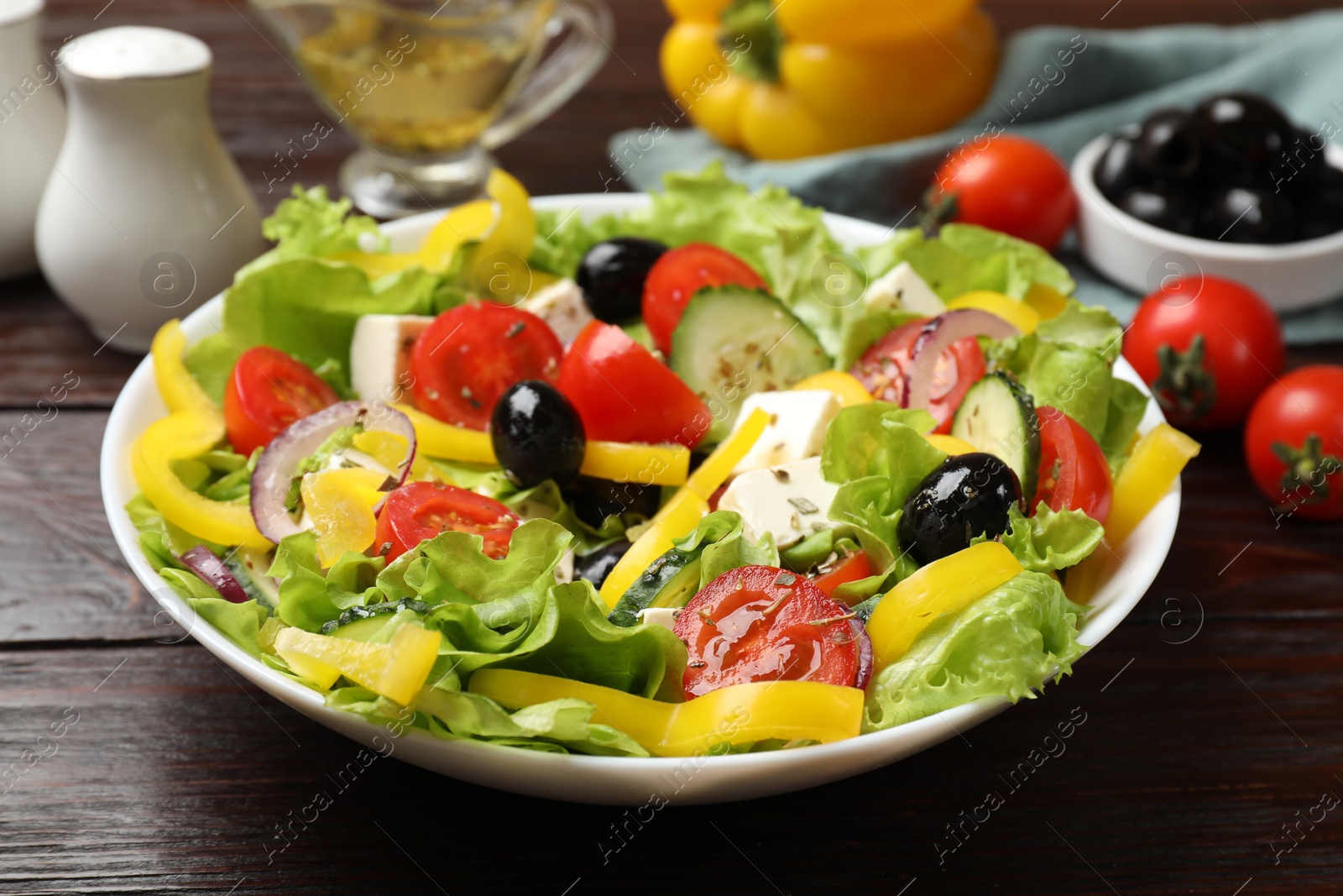 Photo of Delicious fresh Greek salad and ingredients on wooden table, closeup