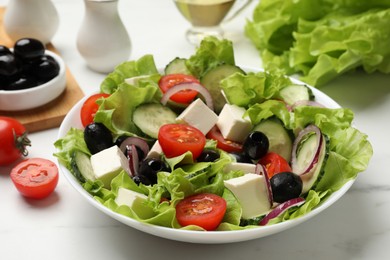 Photo of Delicious fresh Greek salad and ingredients on white marble table, closeup