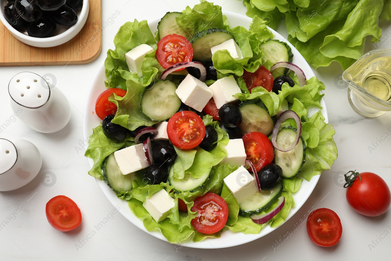 Photo of Delicious fresh Greek salad and ingredients on white table, flat lay