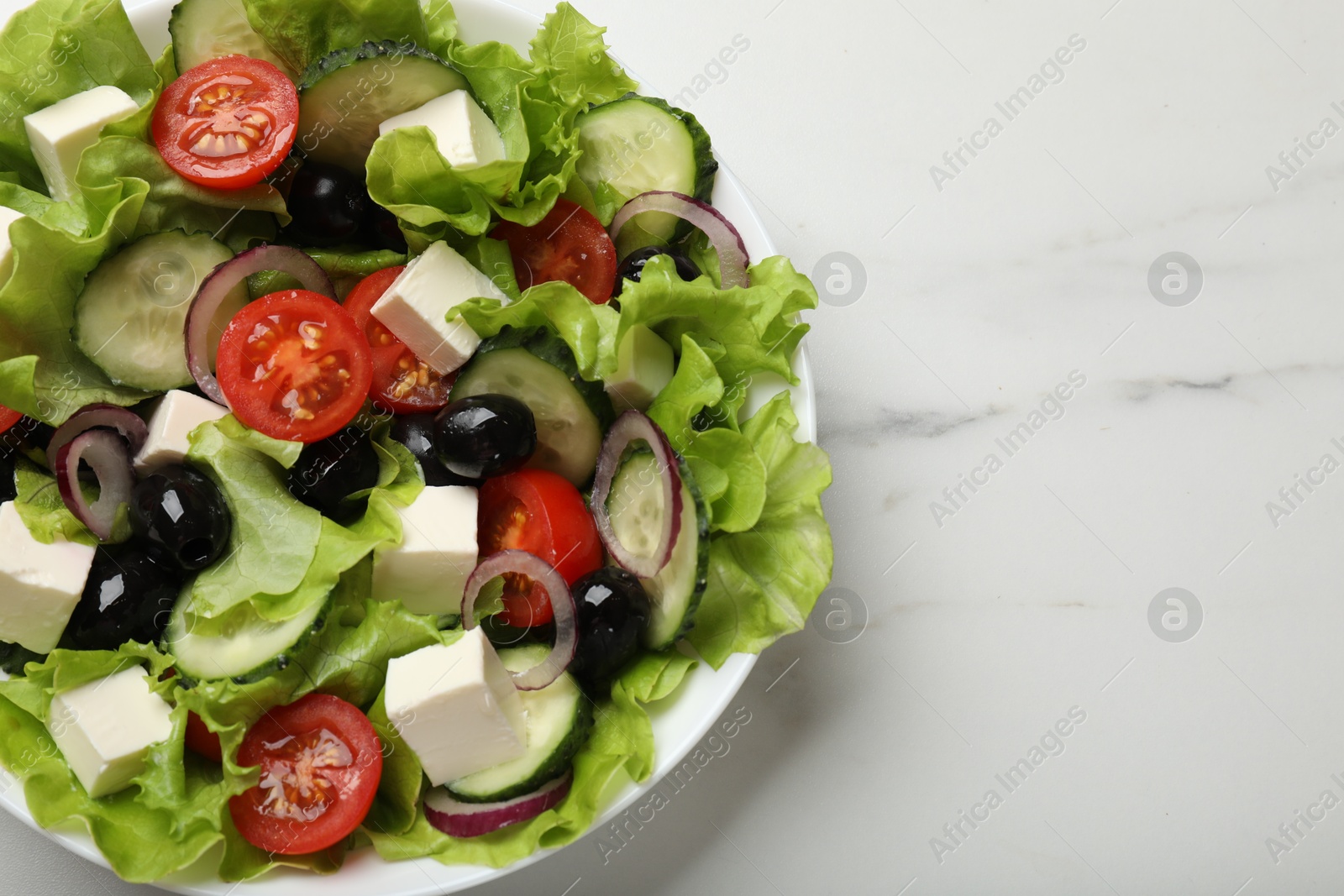 Photo of Delicious fresh Greek salad on white marble table, top view. Space for text