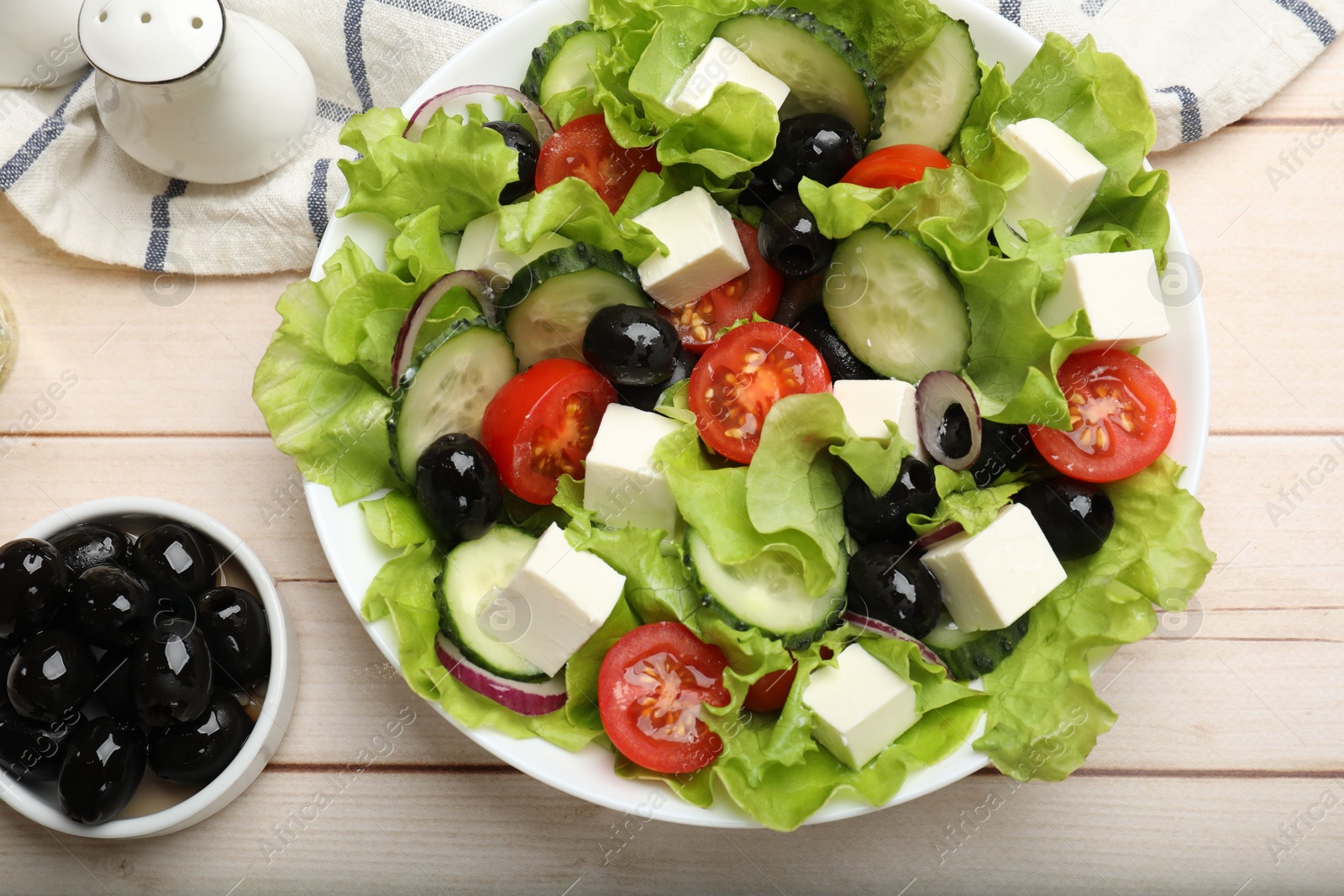 Photo of Delicious fresh Greek salad and ingredients on light wooden table, flat lay