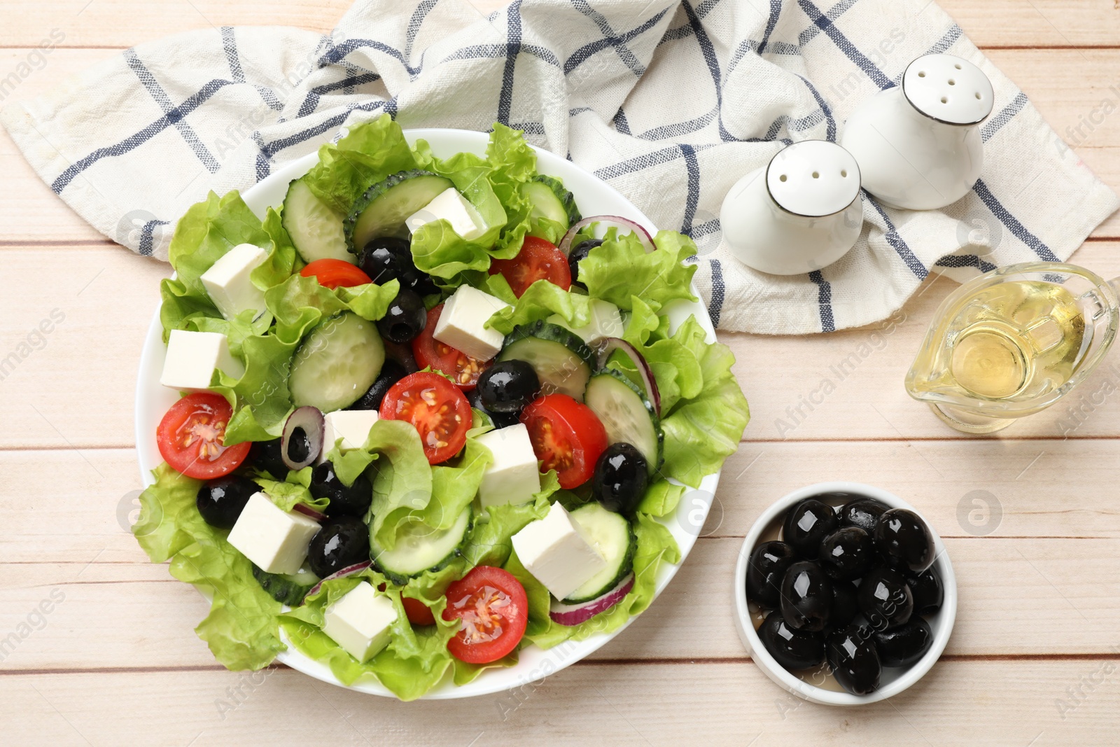 Photo of Delicious fresh Greek salad and ingredients on light wooden table, flat lay