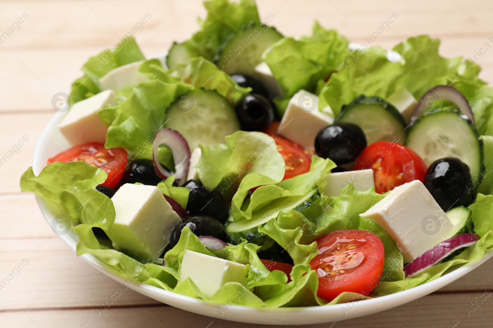 Photo of Delicious fresh Greek salad on light wooden table, closeup