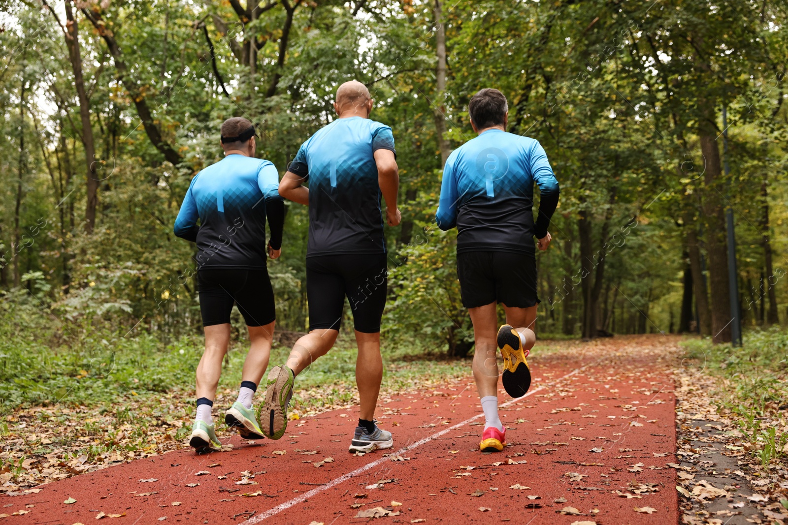 Photo of Group of athletic people running in park, back view