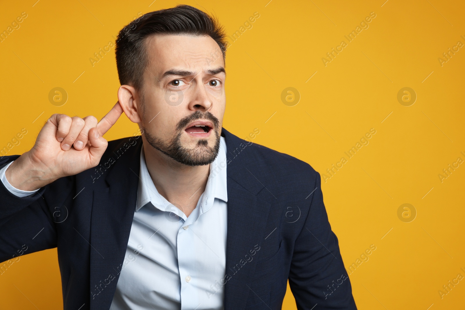 Photo of Man showing hand to ear gesture on orange background