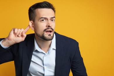 Photo of Man showing hand to ear gesture on orange background