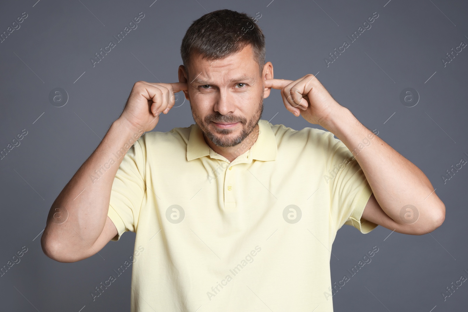 Photo of Man covering his ears with fingers on grey background