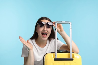 Photo of Woman with suitcase wearing sunglasses on light blue background