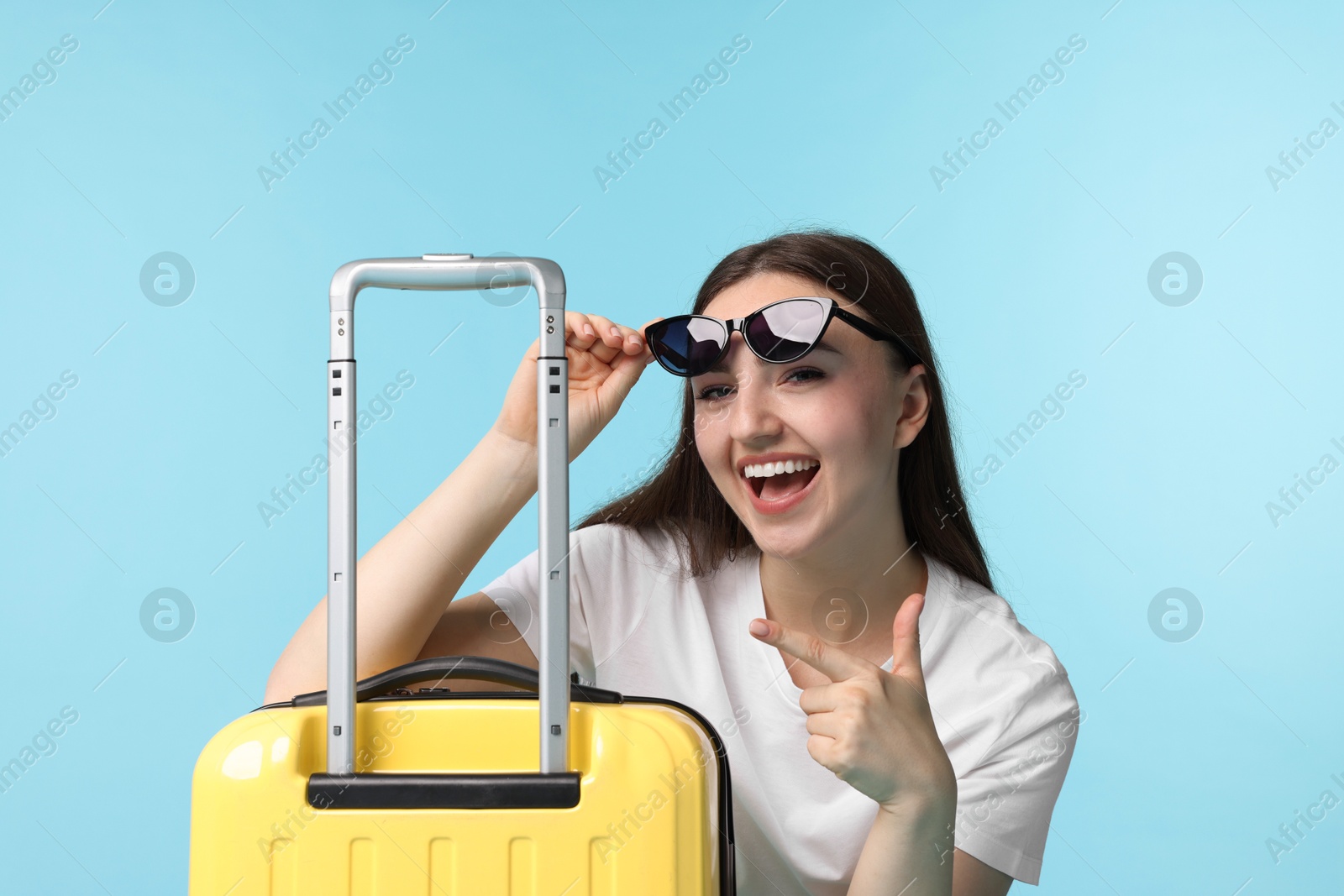 Photo of Woman with suitcase wearing sunglasses on light blue background