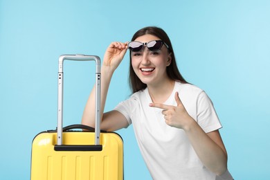 Photo of Woman with suitcase wearing sunglasses on light blue background