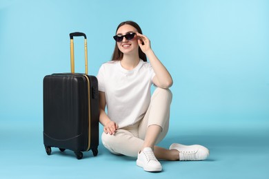 Photo of Woman with suitcase wearing sunglasses on light blue background