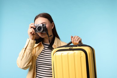 Photo of Woman with vintage camera and suitcase on light blue background