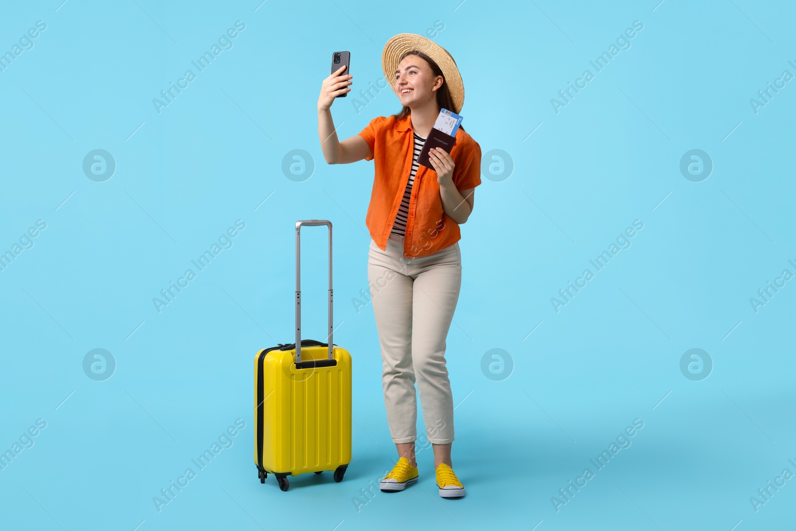 Photo of Woman with ticket, passport and suitcase taking selfie on light blue background