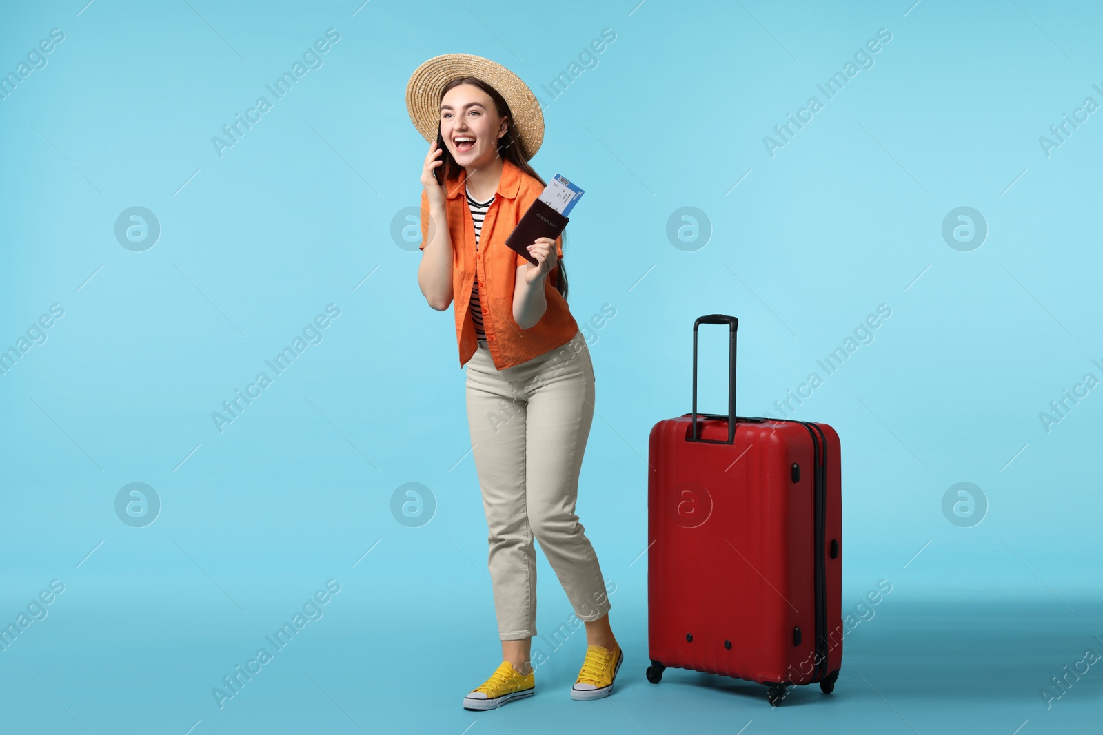 Photo of Woman with ticket, passport and suitcase talking on smartphone against light blue background