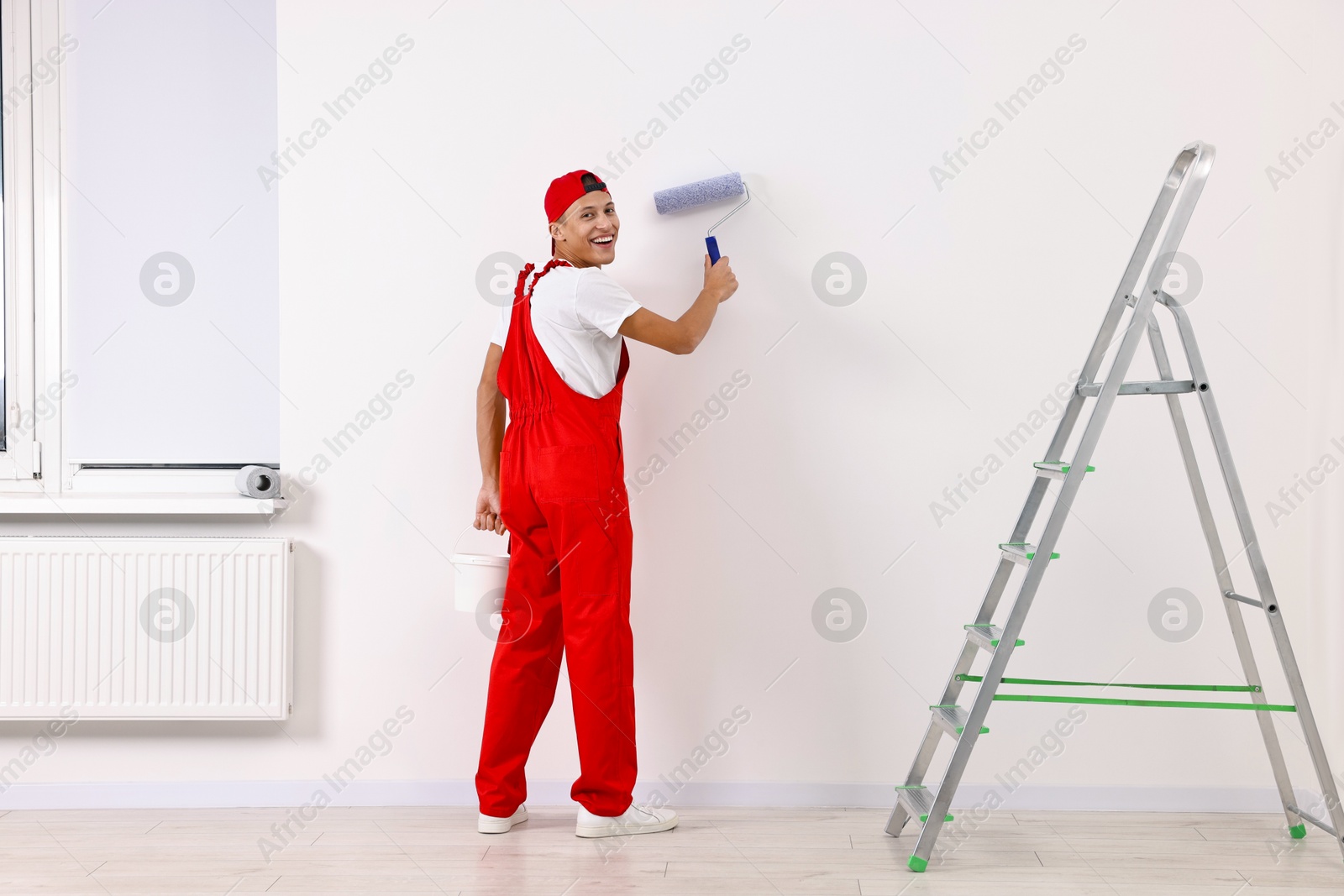 Photo of Smiling handyman painting wall with roller indoors