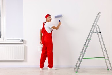 Photo of Smiling handyman painting wall with roller indoors