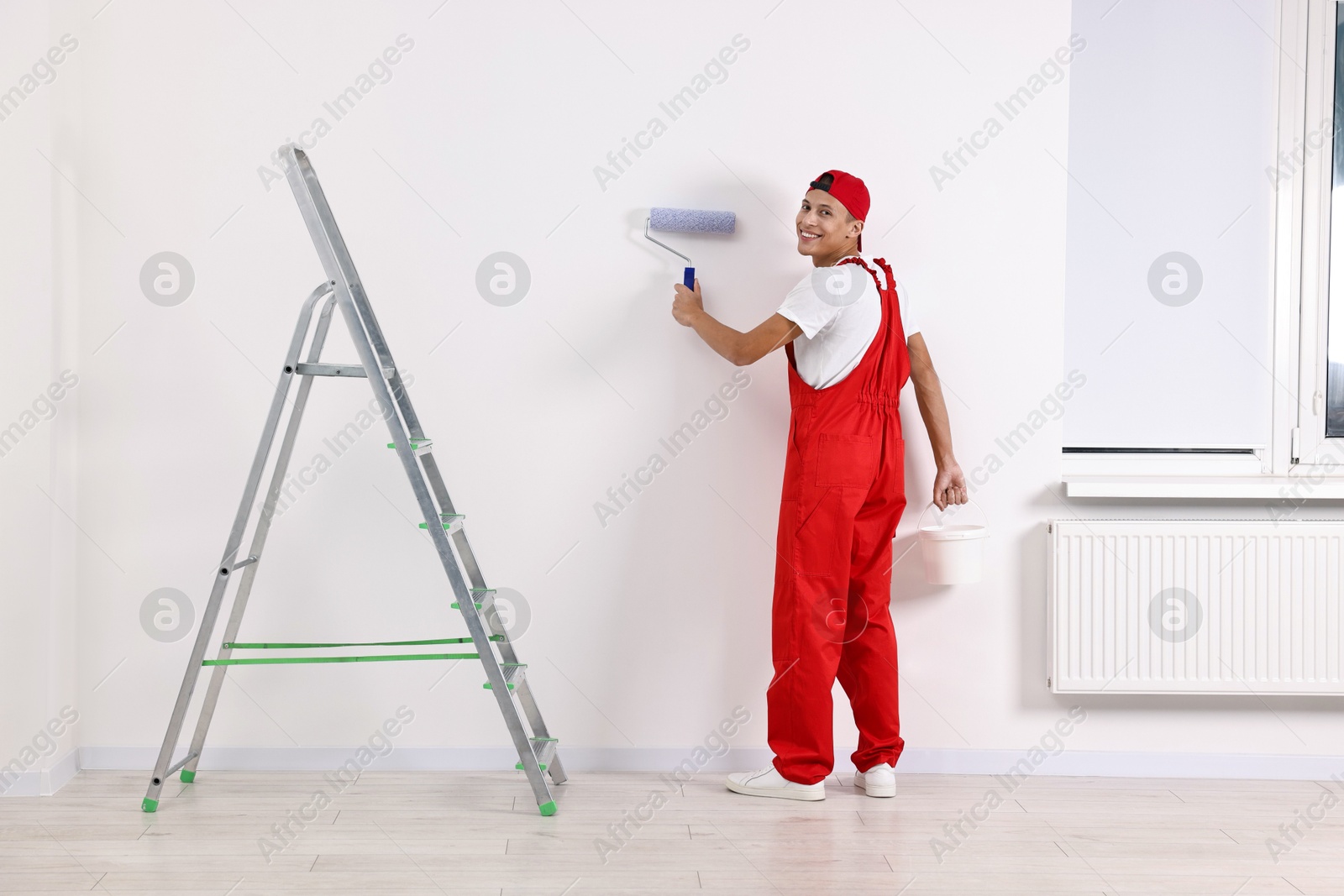 Photo of Smiling handyman painting wall with roller indoors