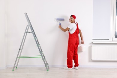 Photo of Smiling handyman painting wall with roller indoors