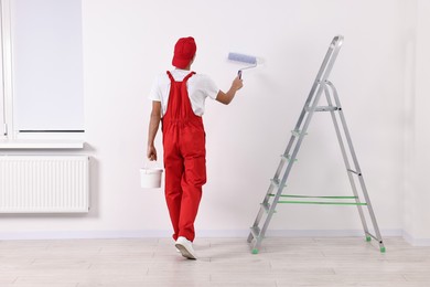 Photo of Handyman painting wall with roller indoors, back view