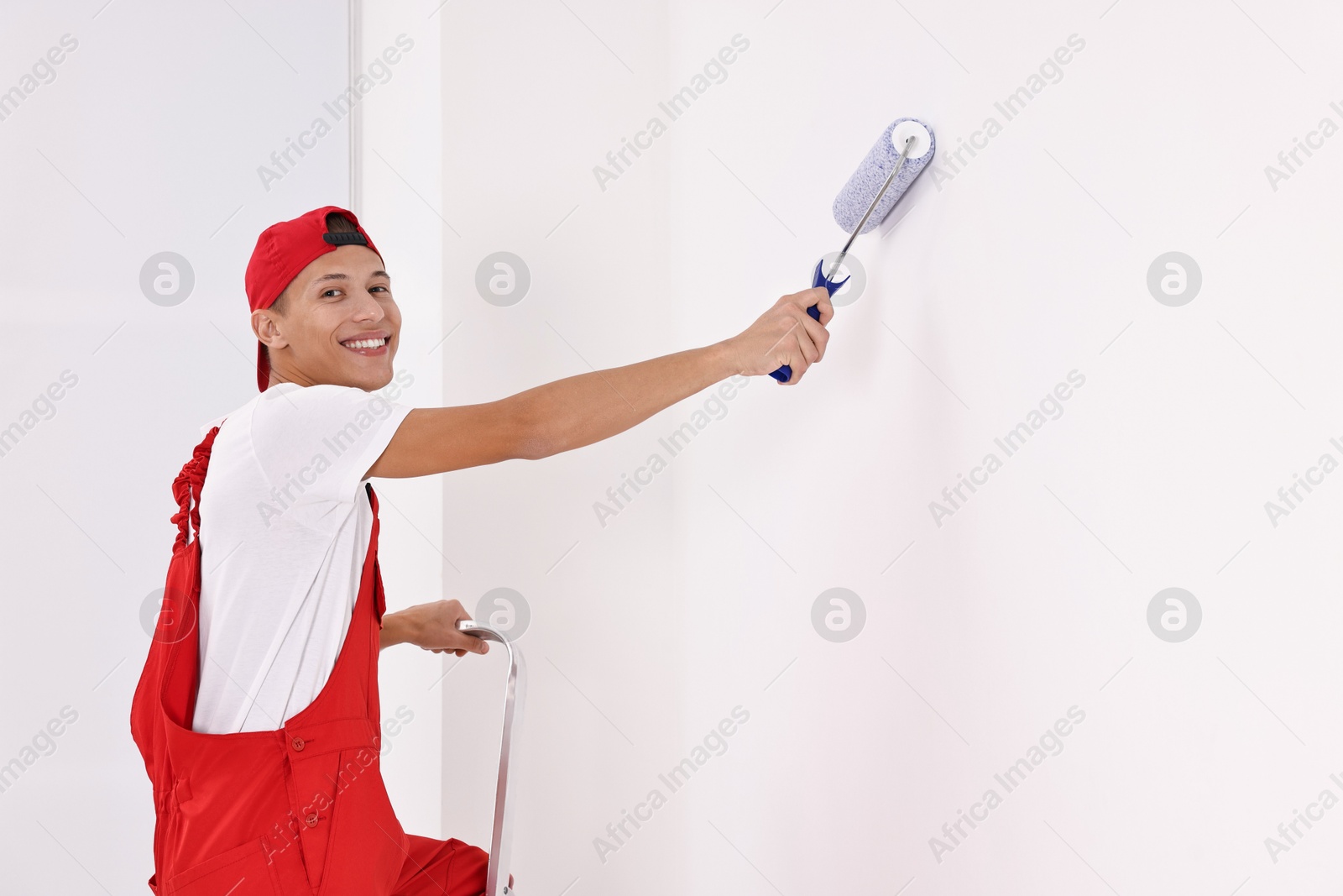 Photo of Smiling handyman painting wall with roller indoors. Space for text