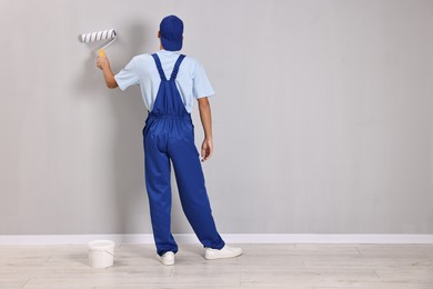 Photo of Male handyman painting wall with roller indoors, back view. Space for text