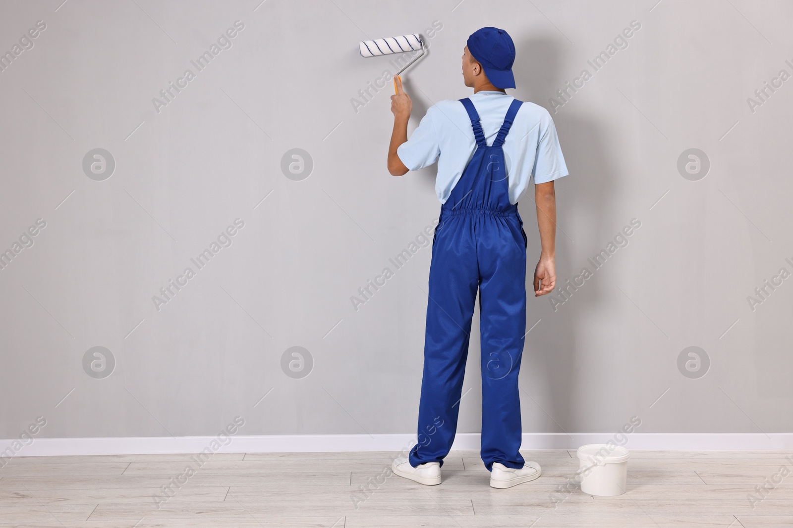 Photo of Male handyman painting wall with roller indoors, back view. Space for text