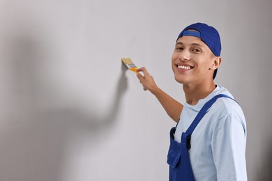 Photo of Smiling handyman painting wall with brush indoors. Space for text