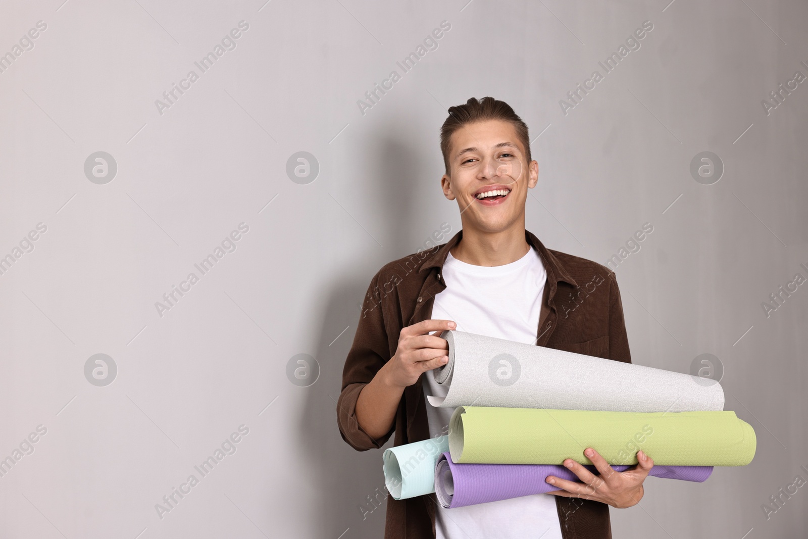 Photo of Smiling handyman with rolls of wallpaper indoors. Space for text