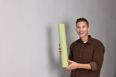 Photo of Smiling handyman with roll of wallpaper indoors. Space for text