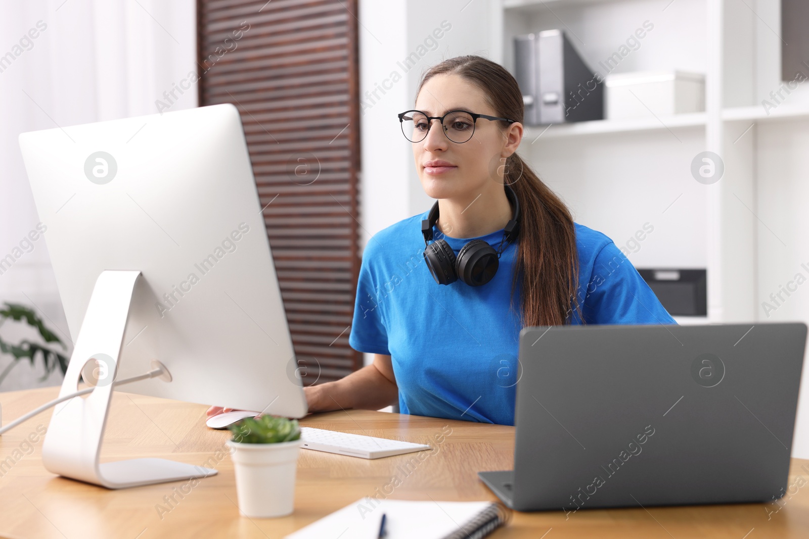 Photo of Programmer working on laptop and computer at wooden desk indoors