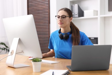 Programmer working on laptop and computer at wooden desk indoors