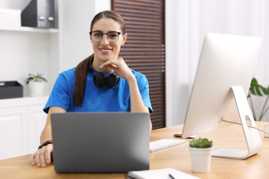 Photo of Programmer working on laptop and computer at wooden desk indoors