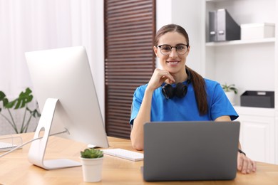 Photo of Programmer working on laptop and computer at wooden desk indoors