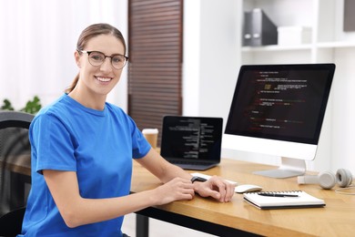 Photo of Programmer working on laptop and computer at wooden desk indoors