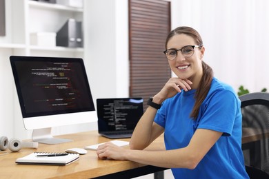 Photo of Programmer working on laptop and computer at wooden desk indoors