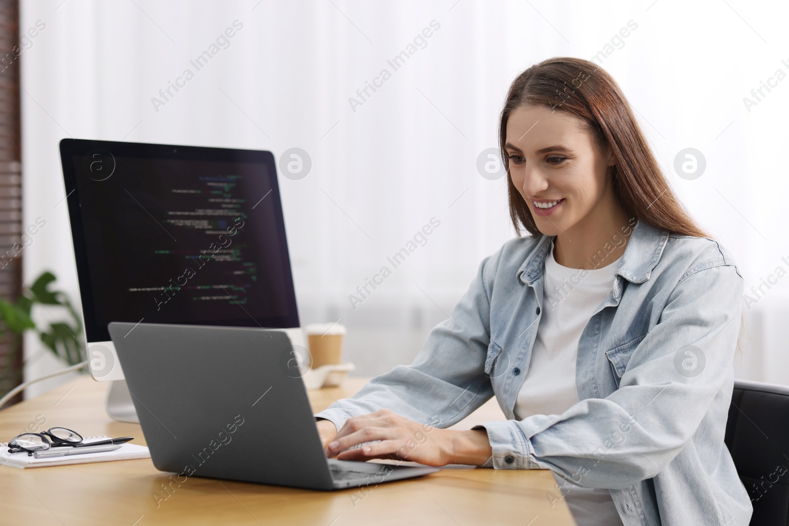 Photo of Programmer working on laptop and computer at wooden desk indoors