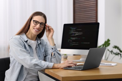 Photo of Programmer working on laptop and computer at wooden desk indoors