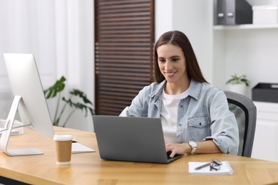 Photo of Programmer working on laptop and computer at wooden desk indoors