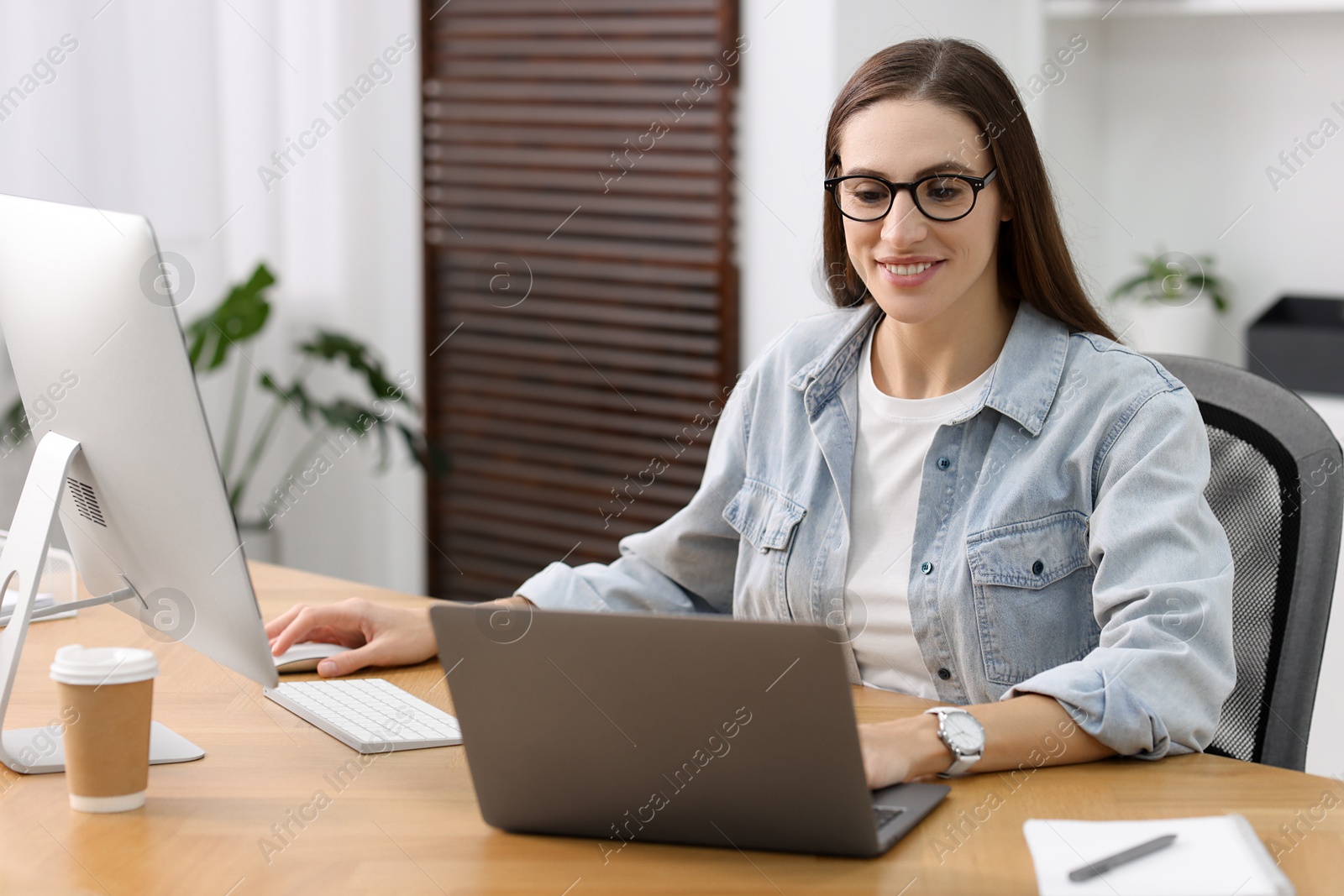 Photo of Programmer working on laptop and computer at wooden desk indoors