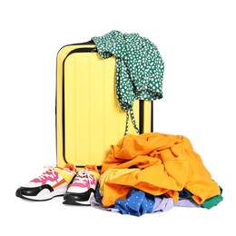 Photo of Yellow suitcase, pile of different messy clothes and sneakers isolated on white