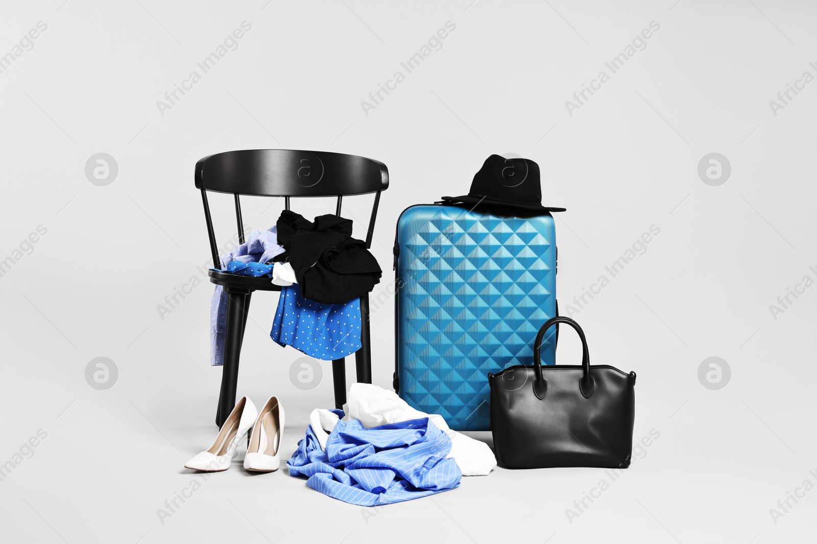 Photo of Suitcase with messy pile of clothes and chair on grey background