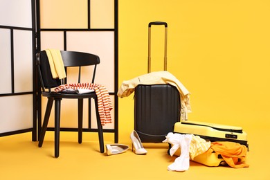 Photo of Suitcase with messy pile of clothes and chair on yellow background