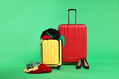 Photo of Suitcases, messy clothes and shoes on green background