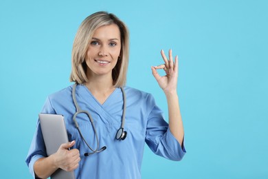 Photo of Doctor with laptop showing okay gesture on light blue background