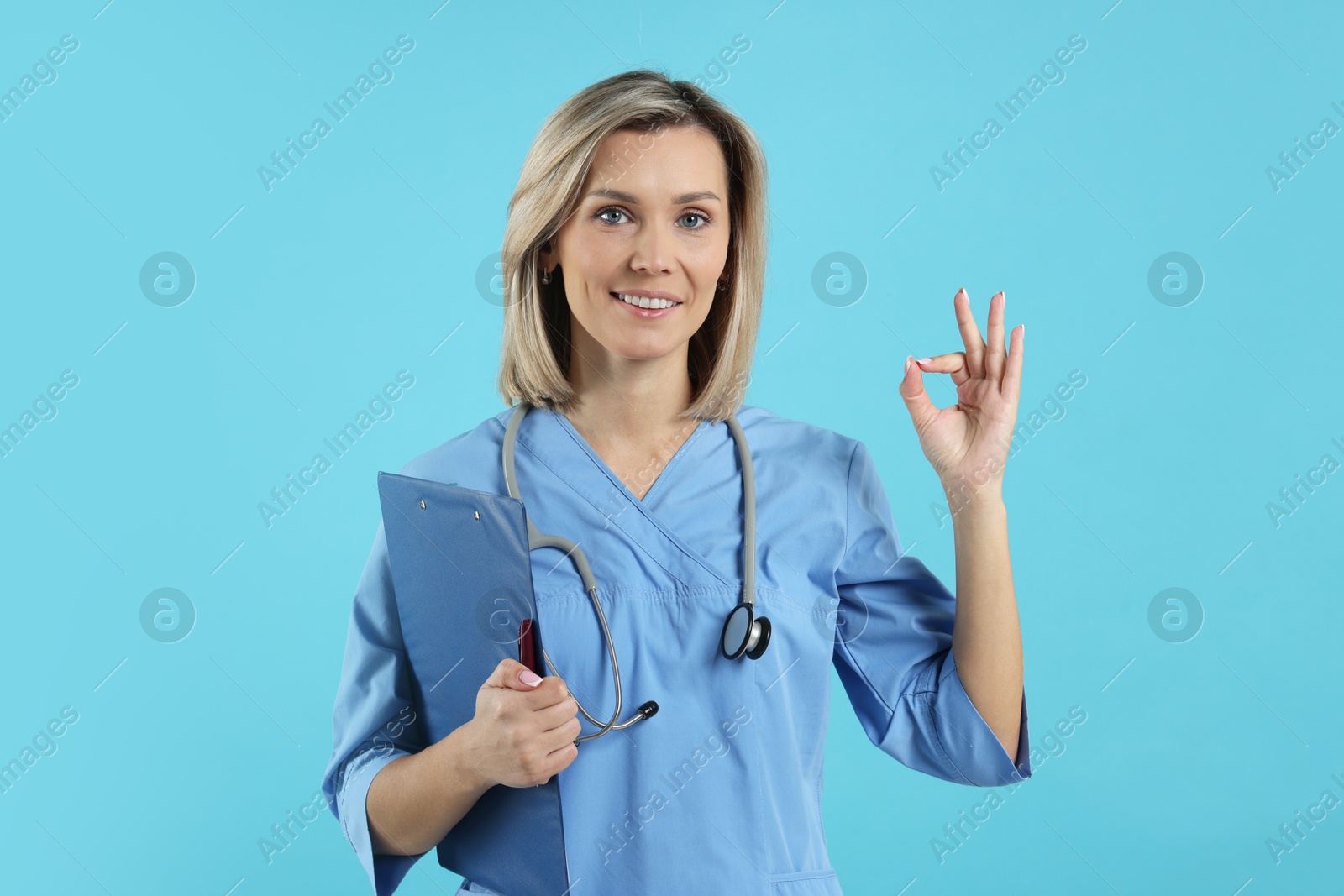 Photo of Doctor with clipboard showing okay gesture on light blue background