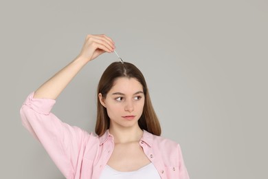 Photo of Hair loss problem. Girl applying serum onto hairline on grey background, space for text